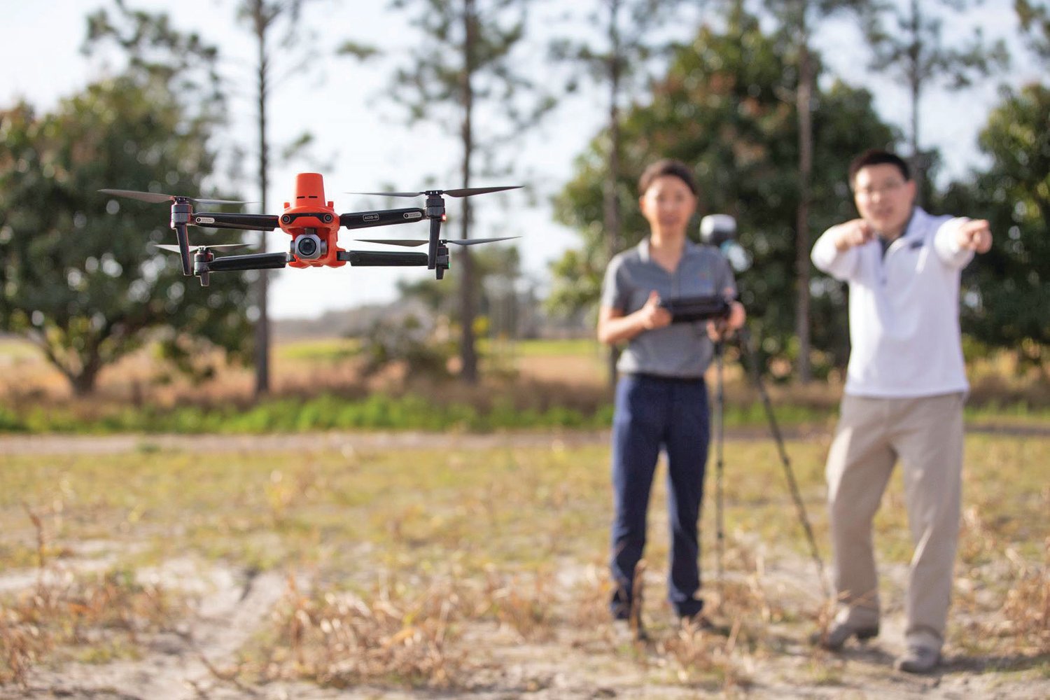 An image of a drone (in focus) at GCREC, with Dana Choi, left, and Kevin Wang in the background. Choi and Wang are both UF/IFAS assistant professors of agriculture and biological engineering at GCREC – and they’re both new faculty hires in AI.